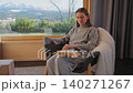 A woman reading by a large window and enjoying scenic snowy mountain view. 140271267