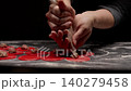 Closeup of chef hands piping meat filling onto circular red pasta dough discs on floured dark 140279458