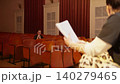 Solitary theater audience member watches performer rehearse with script in empty auditorium rows 140279465