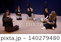 Group of young adults sitting in a circle on a stage floor, sharing conversation and laughter during 140279480