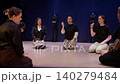 Group of women sitting in a circle on a stage floor practicing interactive theater workshop 140279484