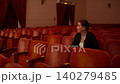Young woman sitting alone in an empty vintage theater auditorium, surrounded by rows of red velvet 140279485