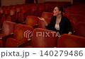 Young woman rehearsing alone in an empty theater auditorium while production crew prepares on stage 140279486