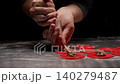 Closeup of chef piping savory meat filling onto bright red dough circles on floured surface in low 140279487