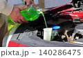 Close-up of hands pouring summer windshield washer fluid into reservoir under car hood, refilling screen wash liquid in engine bay outdoors, car maintenance and care, vehicle service routine, auto 140286475