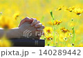 A Christian praying with hands clasped over a holy Bible, against a background of beautiful wildflowers swaying in the wind. 140289442