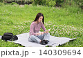 A woman sitting on a picnic blanket outdoors, reading a book. 140309694