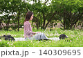 A fixed shot of a woman sitting on a picnic blanket outdoors, looking at her laptop. 140309695