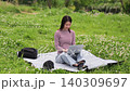 A woman sitting on a picnic blanket outdoors, looking at her laptop. 140309697