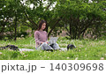 A fixed shot of a woman sitting on a picnic blanket outdoors, looking at her laptop. 140309698