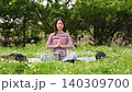 A fixed shot of a woman meditating amidst lush greenery. 140309700
