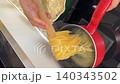 Asian female influencer cooking vlog video using smartphone to film spaghetti alle vongole recipe kitchen showing joyful expression culinary skills boiling pasta with wooden chopsticks pot stove 140343502