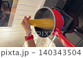 Asian female influencer cooking vlog video using smartphone to prepare spaghetti alle vongole in modern kitchen with red pot showing hand placing pasta into boiling water and cheerful mood 140343504