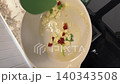 Asian female influencer cooking vlog video using smartphone spaghetti alle vongole recipe showing garlic chili and parsley sauteed olive oil modern kitchen atmosphere with marble countertop 140343508