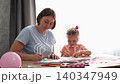 Young mother and child sharing a creative moment while painting and crafting cards. Early learning, family support, and creativity concept. Mid shot. 140347949