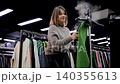 Woman using a clothes steamer and ironing a green jumper in a clothes shop with a stylish modern design 140355613