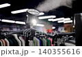 Garment steamer in clothing store producing steam near garment racks 140355616