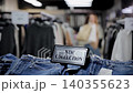 A stylish fashion boutique showcases a new collection of denim jeans and warm sweaters on hangers. Clothing racks in the blurred background create a trendy shopping atmosphere 140355623