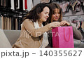 Pretty Caucasian woman surprising her friend by her purchases. Attractive woman emotionally evaluating what her friend has bought. Two female shoppers sharing their impressions from shopping in the 140355627
