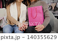 Women share a warm moment holding hands during a shopping outing, showcasing companionship and joy. Girlfriends together in a clothes store 140355629