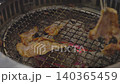 Slices of marinated meat grilling over red-hot charcoal on a wire rack. Metal tongs flip a piece of pork in a traditional Korean BBQ restaurant setting. cooking process. 140365459