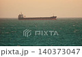 Cargo ship sails on open water during sunset near the coast with waves visible in the background 140373047
