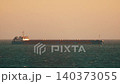 Large cargo ship sails across wide ocean during sunset in distant view of the horizon 140373055