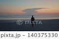 Silhouette of graceful lady walks along sunrise ocean beach against cloudscape. Dark woman figure with mat for exercising rests at tranquil exotic resort 140375330