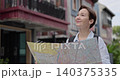 Portrait of woman traveler reads map and smiles standing in old downtown. Female with backpack observes landmarks as holds city plan against ancient buildings 140375335