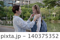 Portrait of happy mother kisses little daughter and sets backpack in autumn park. Woman cares of girl junior student ready for school in public garden 140375352