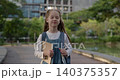Portrait of happy junior schoolgirl walks alone across autumn park. Little girl student with backpack and notepad smiles on way to school in city garden 140375357