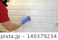 Thoroughly cleaning the grout between tiles. Manually cleaning stains on white tiles. Close-up of a gloved hand cleaning white tiles. A variety of tile cleaning products. The problem of cleaning. 140379234