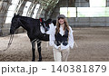 Woman with flat cap and black horse in riding arena 140381879
