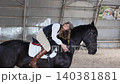 Woman wearing cap petting black horse in stable 140381881