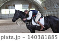Young woman embracing black horse in indoor arena 140381885