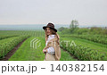 Woman walking through green agricultural field wearing a hat 140382154