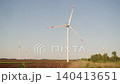 Wind turbines rotate slowly across rural farmland under clear blue sky. Scenic landscape shows renewable energy production in peaceful countryside. 140413651