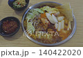Traditional Korean spicy hot pot in a metal pan with cabbage, mushrooms, kimchi, and rice cakes. Served on a wooden table with chili sauce and garlic condiments. Authentic Asian cuisine concept. 140422020