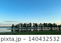A tranquil lake at sunset with reflections of trees and blue sky, a peaceful summer landscape with nature as a backdrop. 140432532