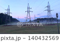 High voltage power lines in a foggy field at dawn, power line pylons and energy infrastructure landscape. 140432569