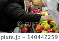 Young woman is choosing fresh bell peppers from a supermarket shelf and putting them into a plastic bag. She is shopping for groceries 140442259