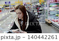 Young woman selecting frozen food items from a supermarket's refrigerated aisle. Various products are available, showcasing options for healthy meals and snacks 140442261