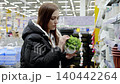 Customer examining a green artificial plant in a pot while shopping in a supermarket. Holding the plant, she evaluates its features and considers options for home decor 140442264