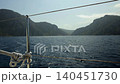 Onboard video from a fast-moving boat with iron railings onto calm water and mountains on the shore of a sea bay 140451730