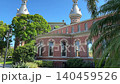 A circular wing of the historic university building displays classic Victorian brickwork and large arched windows. Lush green shrubs and palm trees surround the paved courtyard on a sunny Florida day. 140459526