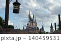 An ornate black lamp hangs from a wooden post in the foreground with a towering magical palace behind it. Soft sunlight filters through white clouds over the iconic spires and blue turrets of the 140459531
