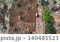 Aerial drone shot of a red tractor working on tilled brown soil in rural Turkey, surrounded by green trees and natural landscape. 140485523