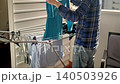 A person hangs clean clothes on a drying rack inside a room. The task takes place in Villajoyosa, Spain, where sunlight fills the space. The clothes are neatly organized as they dry. 140503926