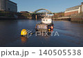 Low-altitude aerial drone shot tracking around a small blue boat moored on the River Wear, revealing the Wearmouth Bridge and Monkwearmouth Railway Bridge in Sunderland. 140505538