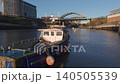 Low-altitude aerial tracking shot passing a small weathered boat moored on the River Wear, with the Wearmouth Bridge and Monkwearmouth Railway Bridge in the background in Sunderland. 140505539